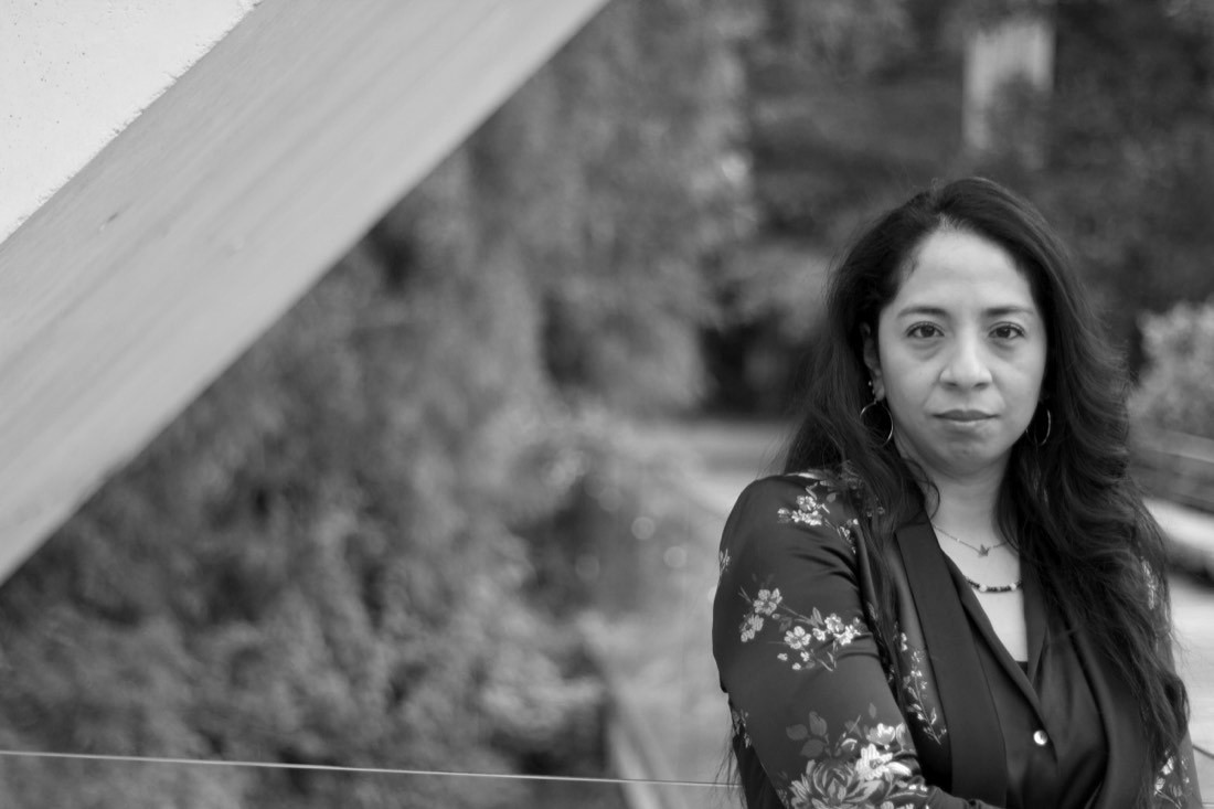 Retrato de Azucena Meza Uscanga recargada en un barandal, con vegetación al fondo.